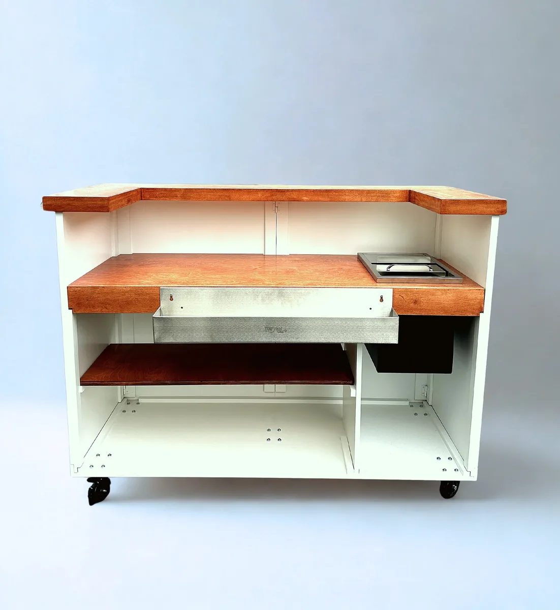 A white cart from the service side, with a stained wood top, open shelving and a stainless well