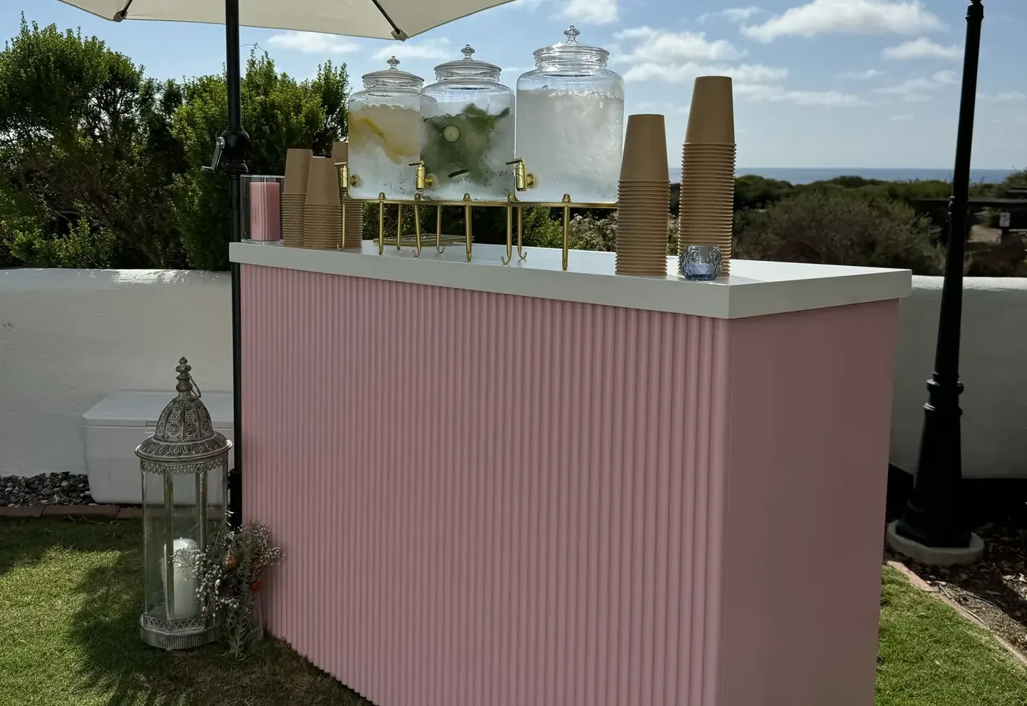 A pink fluted RidgeCraft bar set up for an event on a coastal patio, with drink dispensers and cups on top