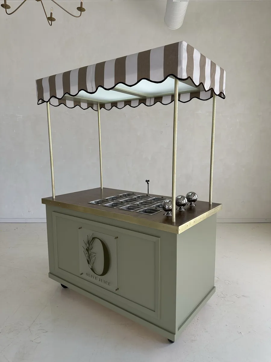 A sage green awning cart with brass posts and a striped canopy