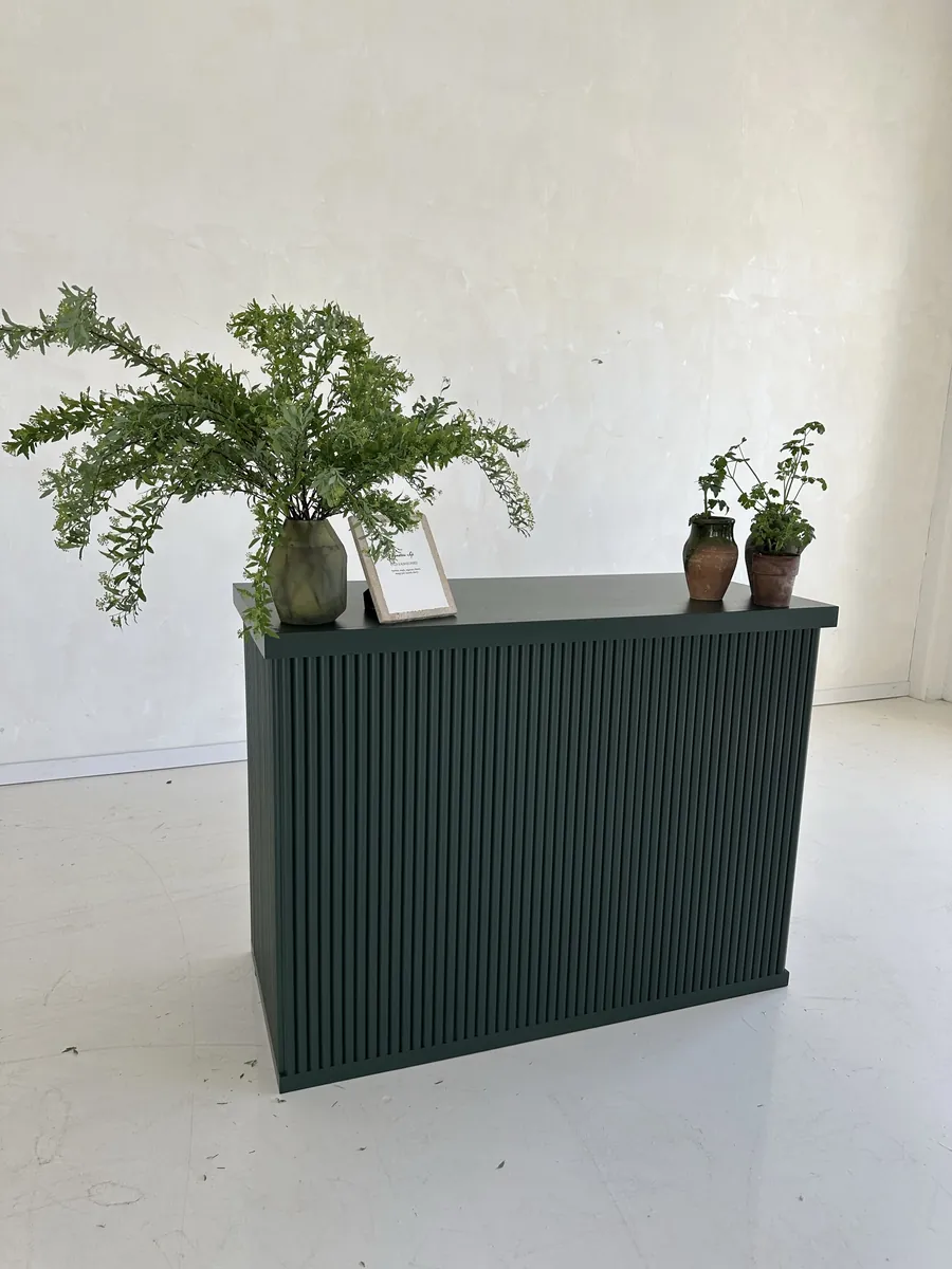A bar with a fluted front painted forest green, in a studio