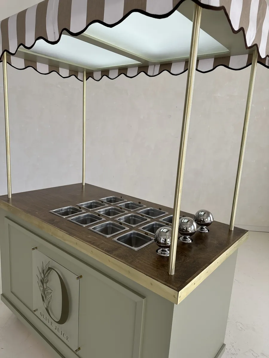 Close up of a sage green awning cart: a walnut top with brass trim and a grid of stainless wells